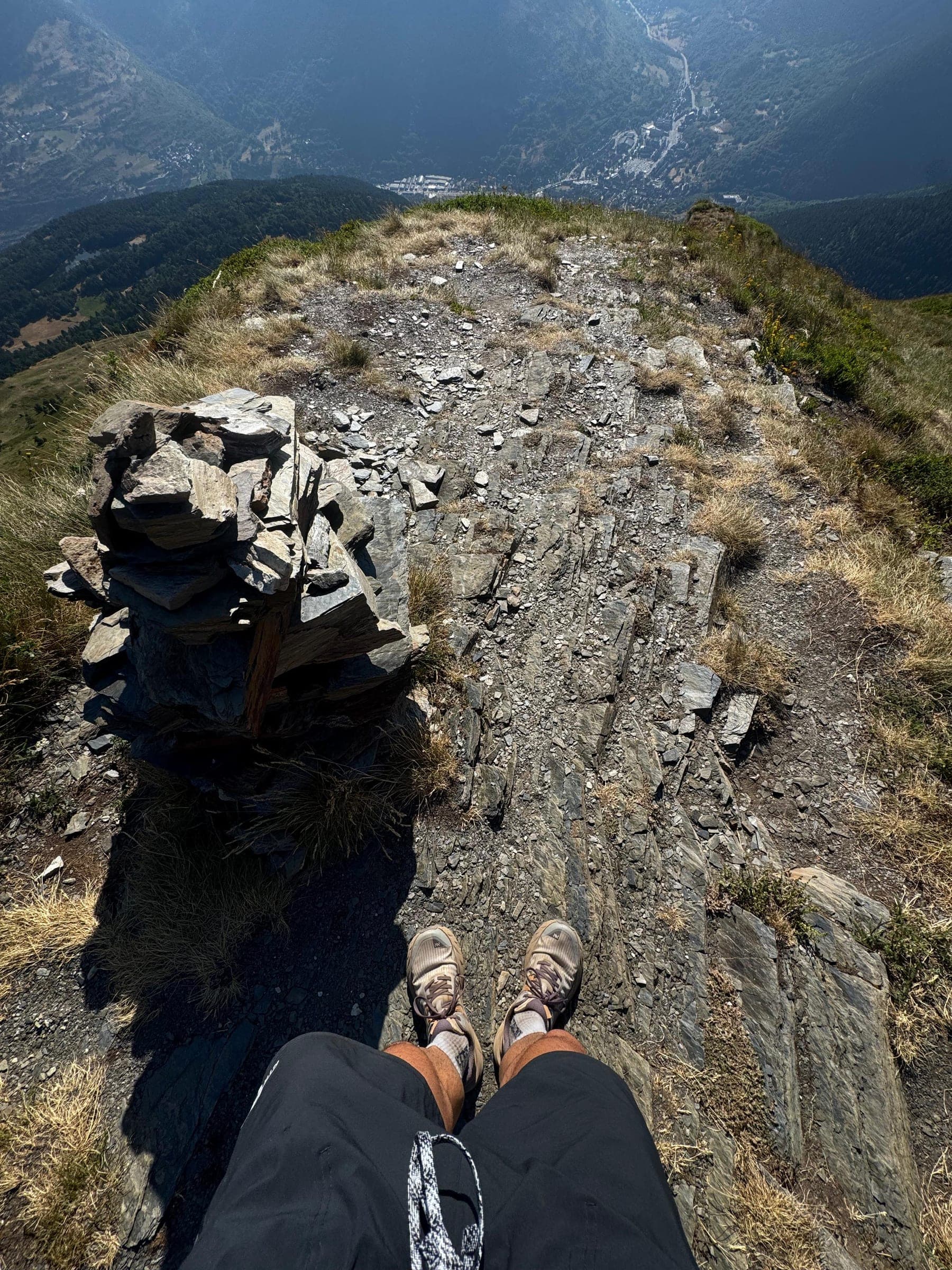 Pies sobre un mojón de piedras en la cima, con un valle y un pueblo muy abajo