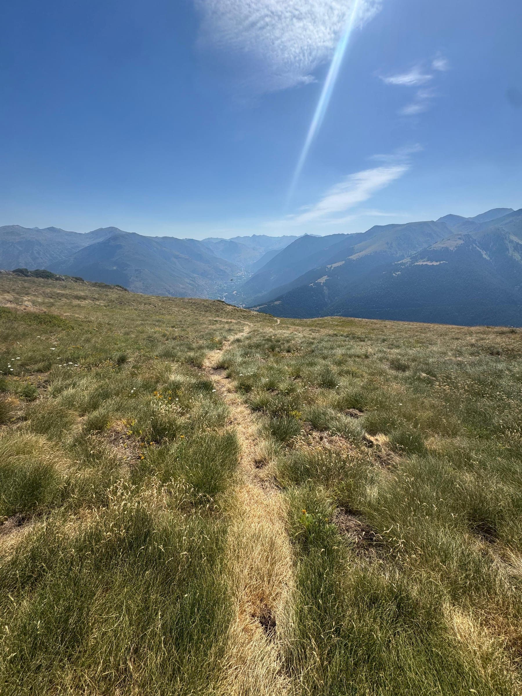 Sendero de hierba en una cresta con montañas al fondo bajo un cielo despejado