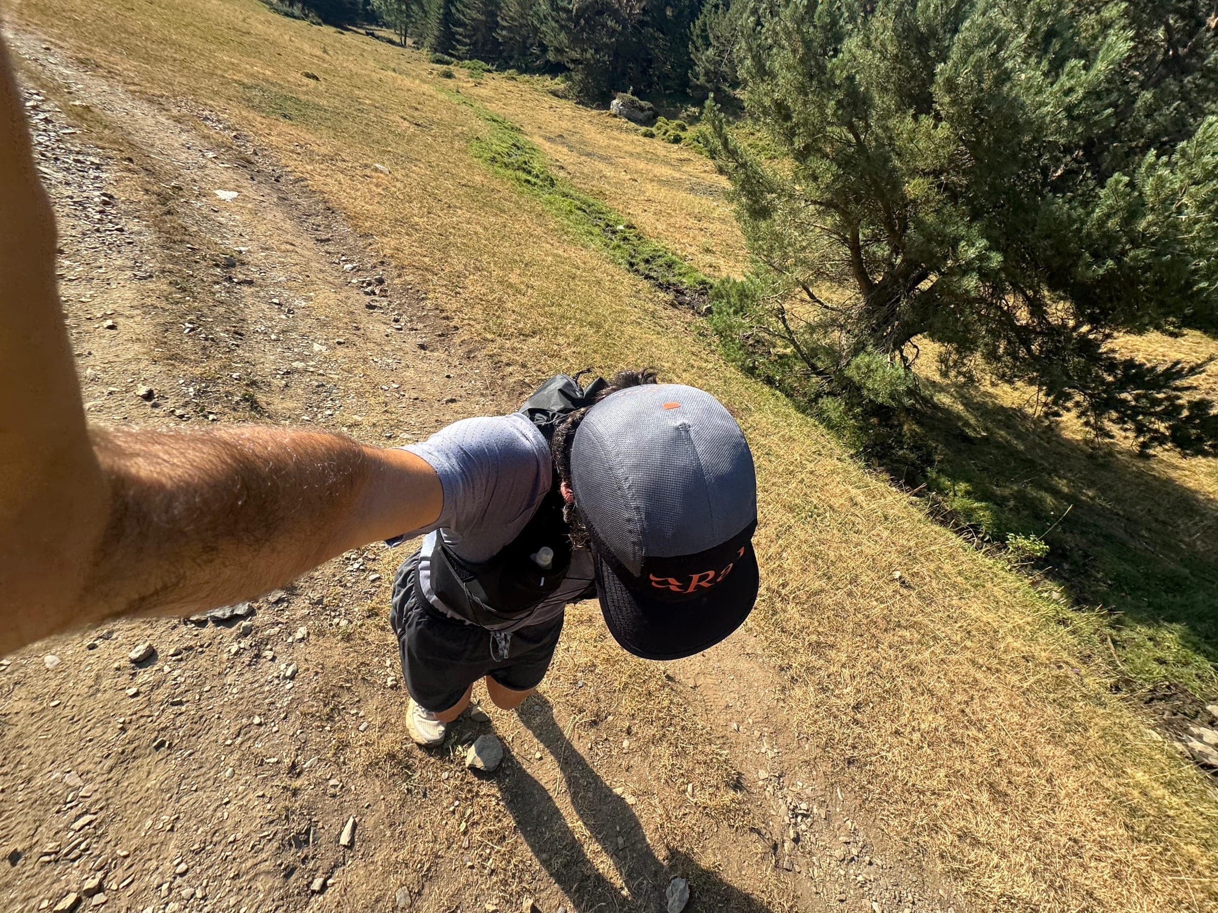 Corredor con gorra y mochila de trail bajando por una pista de tierra entre pinos