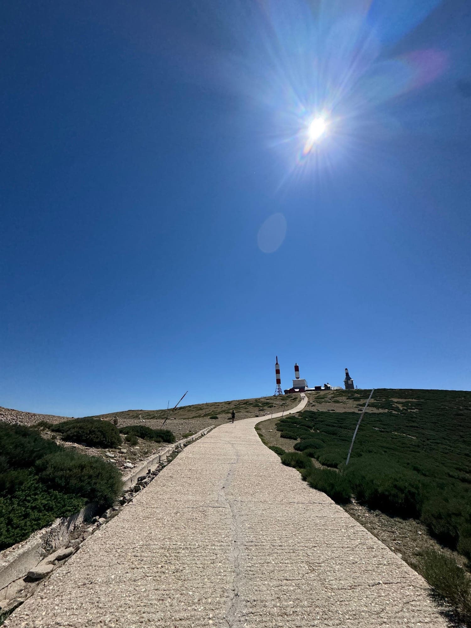 Camino de hormigón hacia la cima de la Bola del Mundo, con antenas al fondo bajo el sol