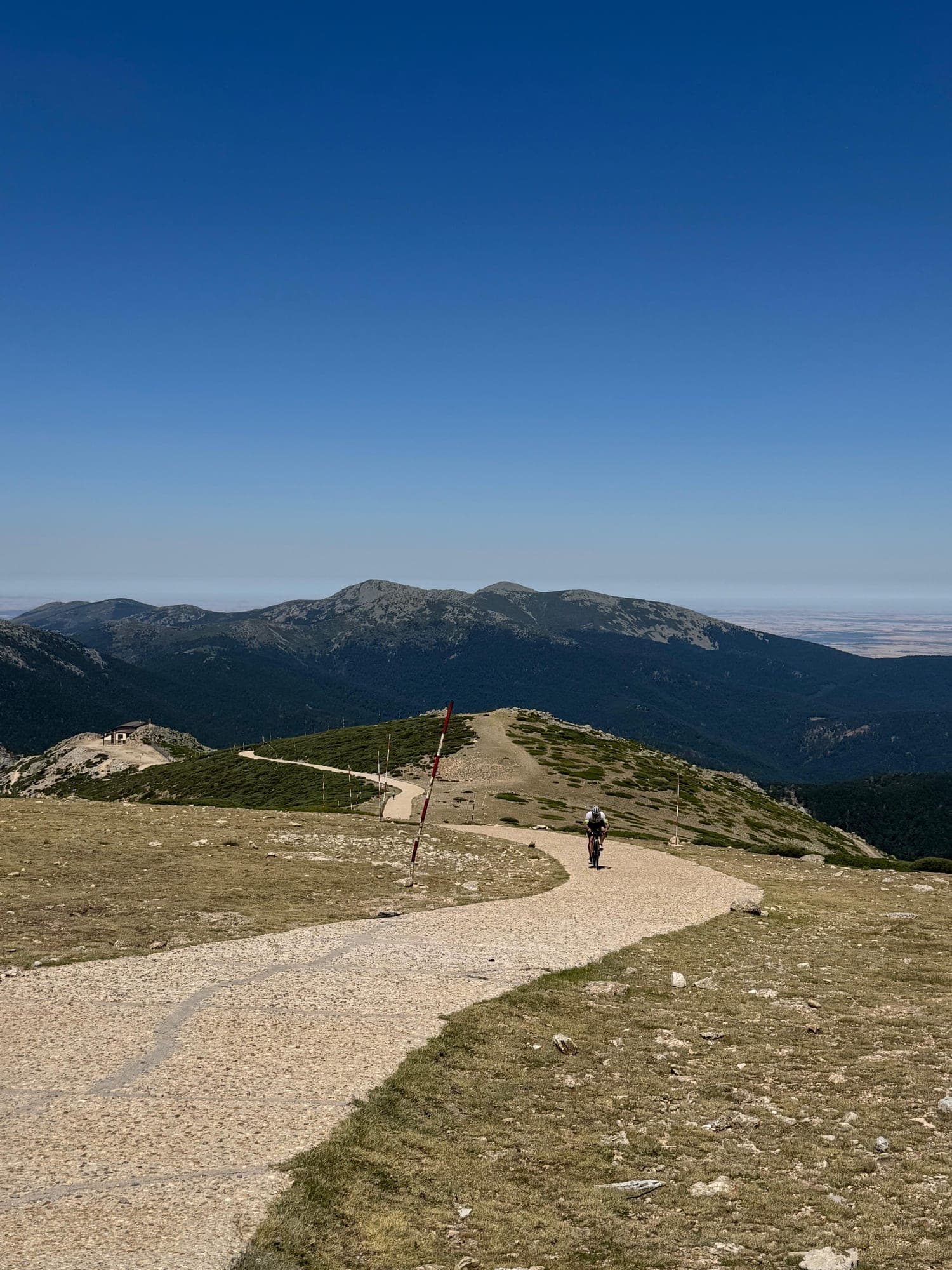 Ciclista subiendo en solitario cerca de la cima, con un refugio al fondo